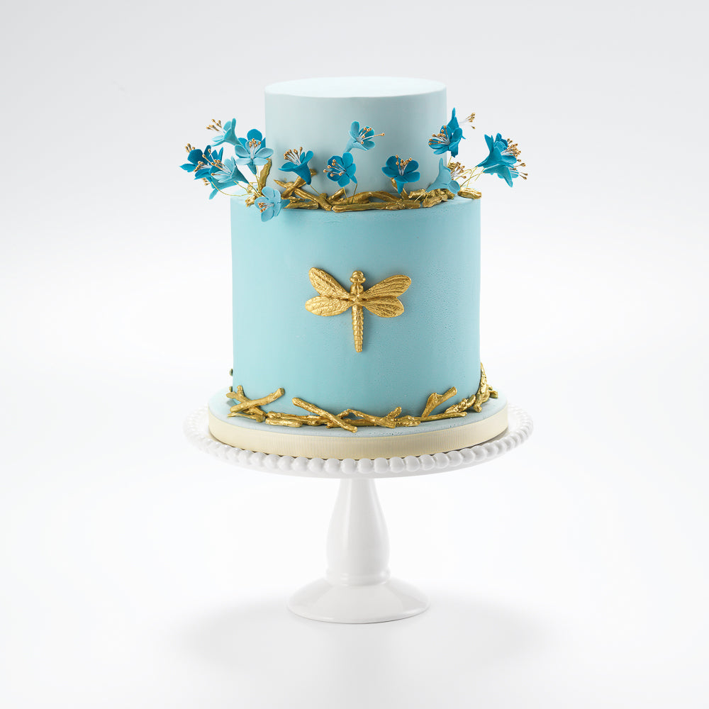 Golden sugar paste twigs litter the bottom tier of this golden dragonfly celebration cake, ideal for a birthday cake. While lovingly crafted edible sugar flowers grow out, like a wild meadow, from soft blue iced fondant.