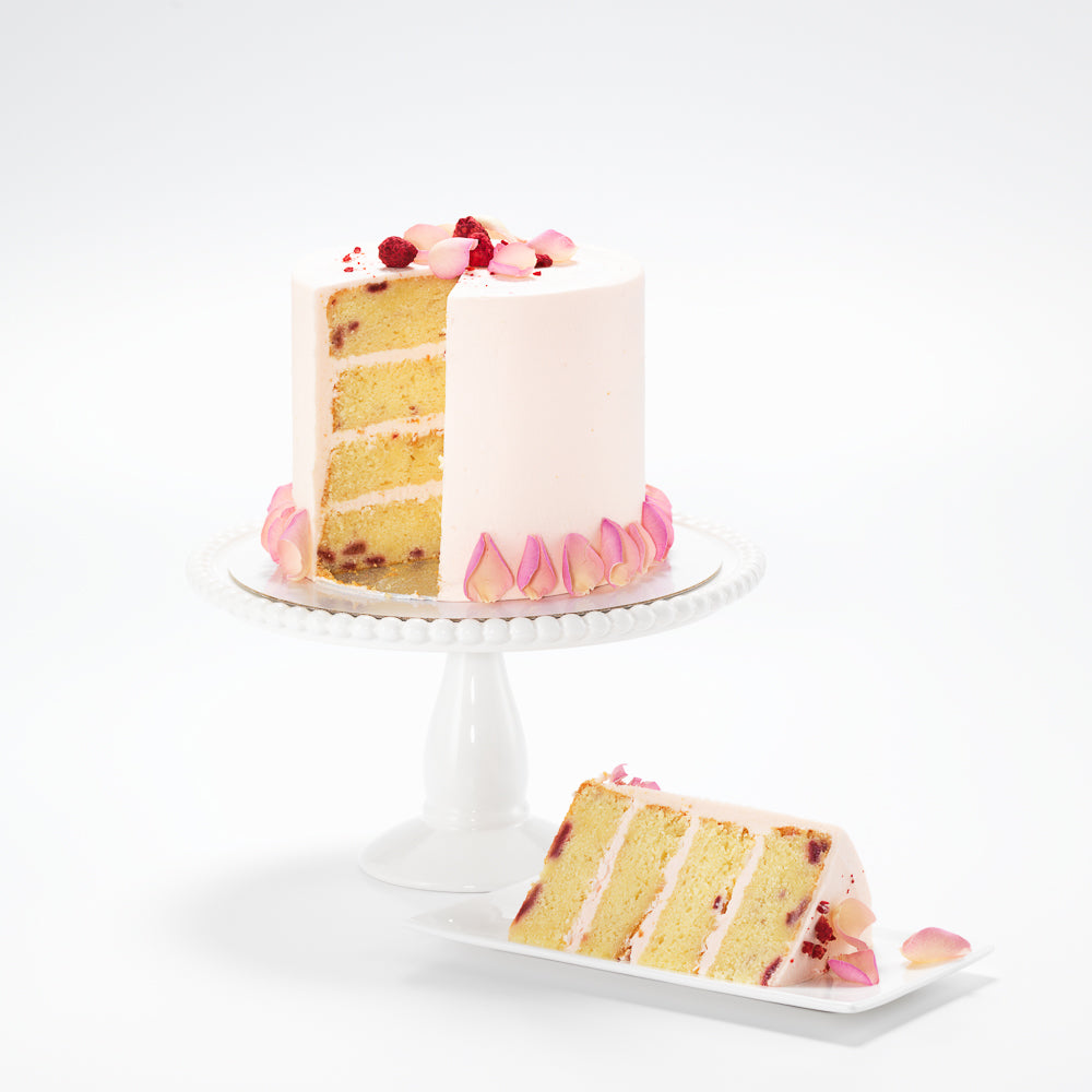 A delicately decorated raspberry and rose cake. Its rich, raspberry sponge is perfectly complimented by subtle, rose buttercream.  While the rose buttercream icing is graced with edible candy pink rose petals and a sprinkle of freeze-dried raspberries.